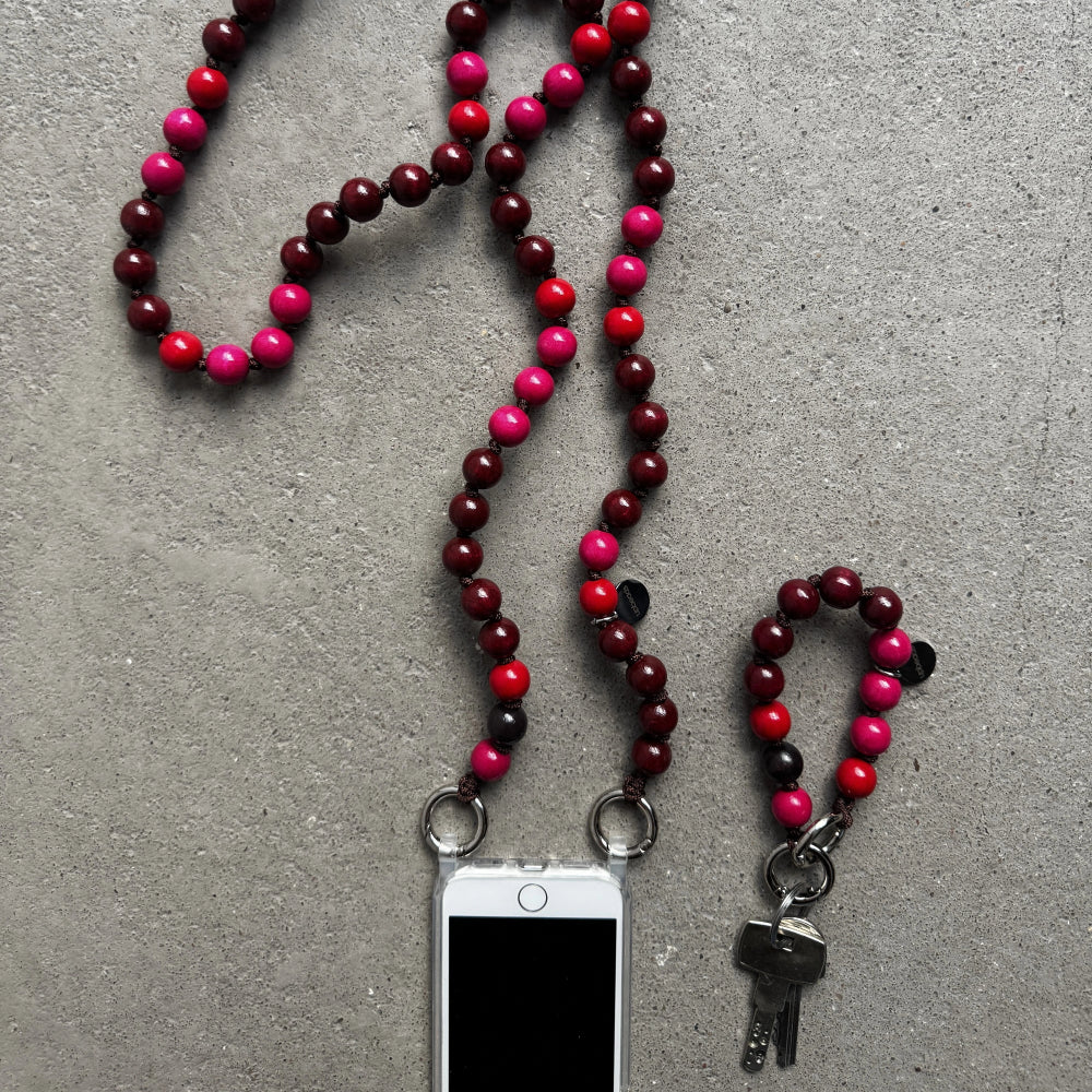 A beaded phone strap and keychain set made of alternating dark red and bright pink and red beads, shown on a gray textured surface with a smartphone and keys attached.