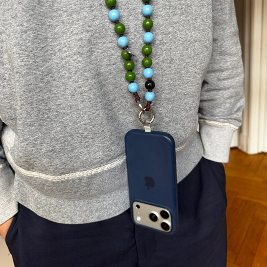 Person wearing a gray sweater with a blue phone case with an adapter on a green and blue wooden beaded upbeads.