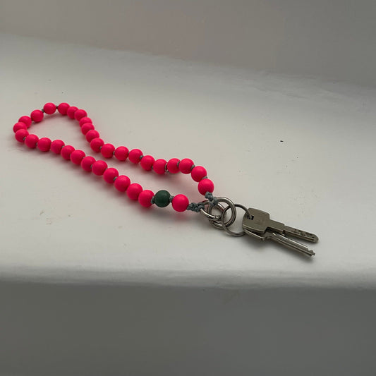 upbeads wooden bead chain used as a keychain the color is bright neon pink with a signature bead in sage green