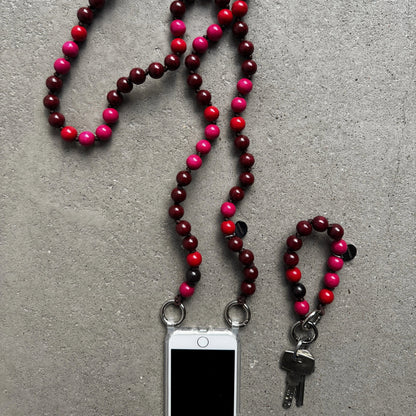 A beaded phone strap and keychain set made of alternating dark red and bright pink and red beads, shown on a gray textured surface with a smartphone and keys attached.