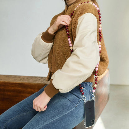 Person wearing a brown vest with a beaded necklace, sitting on a wooden bench.