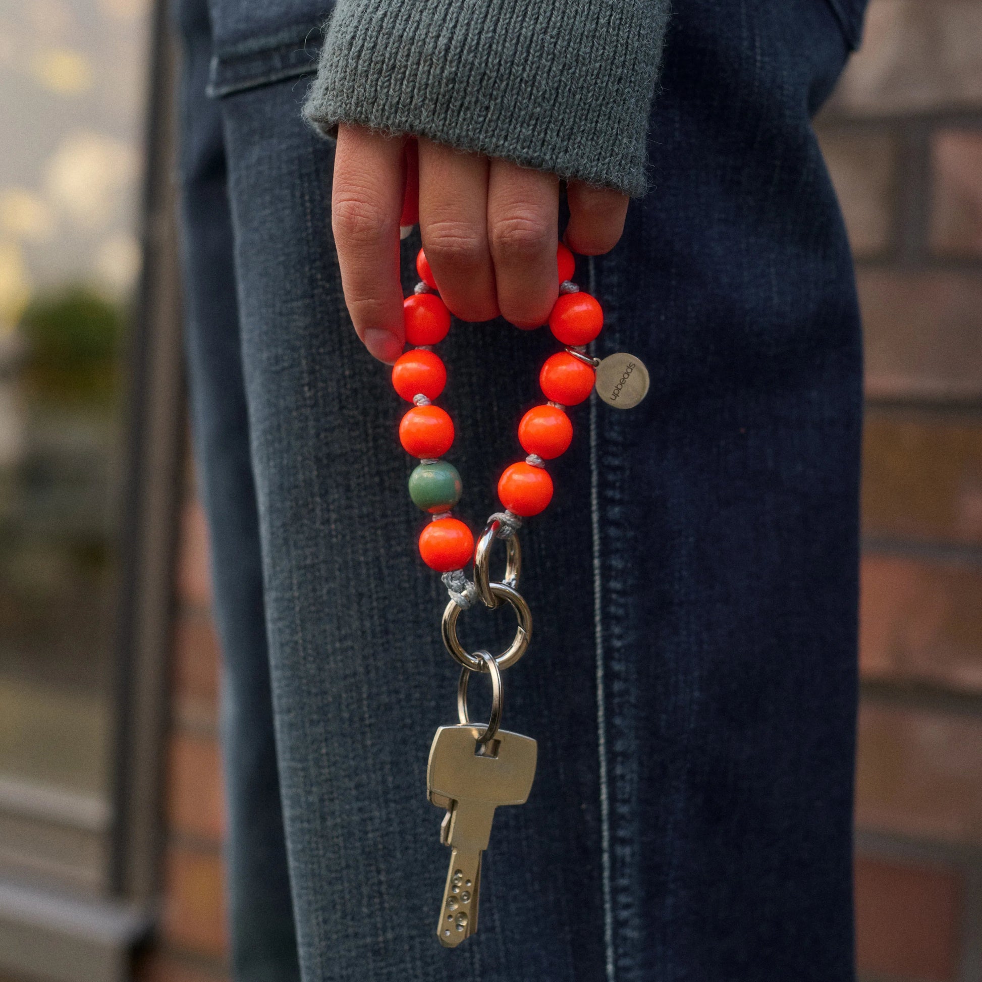 model holds upbeads mini foxy in neon orange wooden beads as a keychain