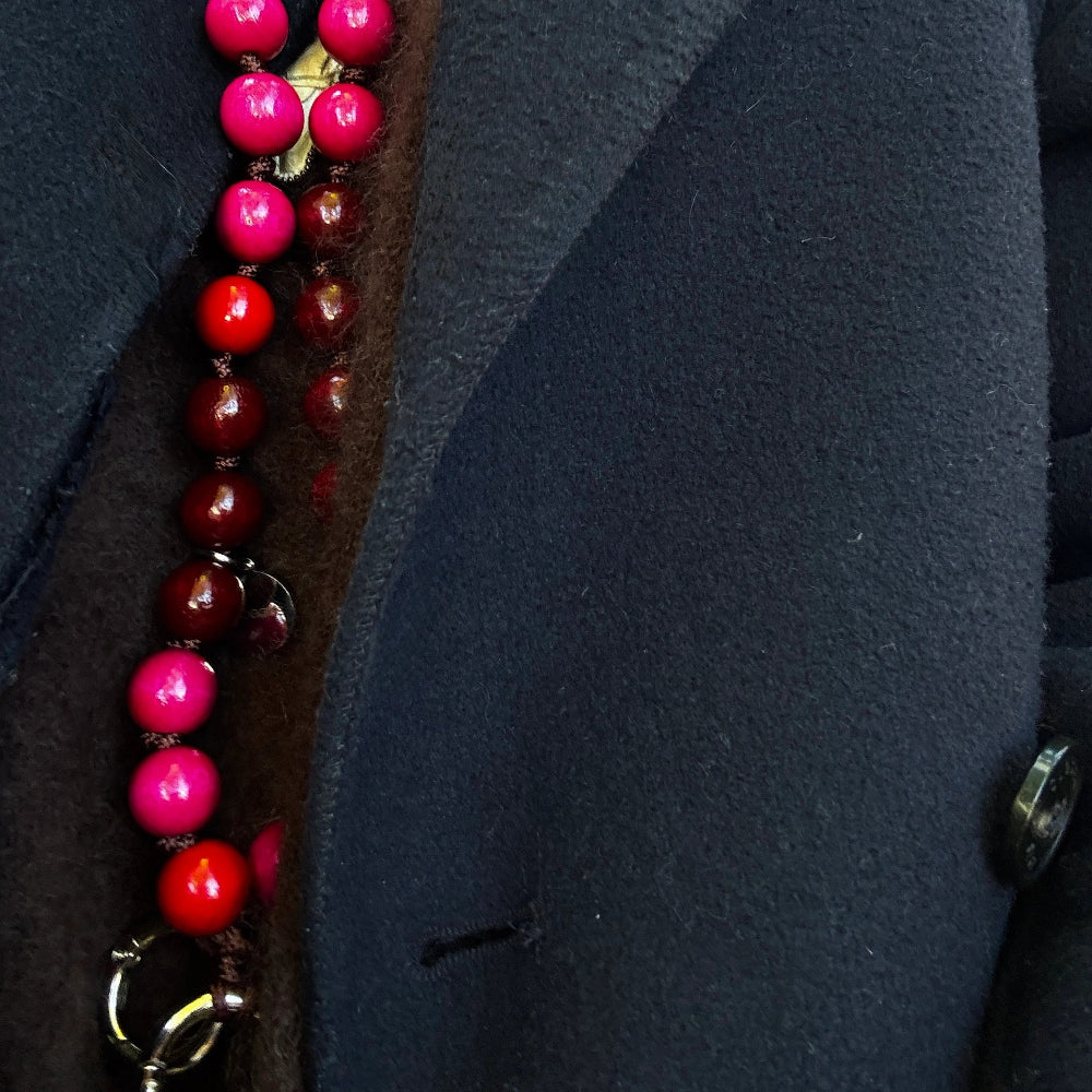 upbeads cellphone chain mixture of bordeaux, brigth pink and red FSC wooden beads worn as a necklace on dark brown cashmere sweater and dark blue jacket