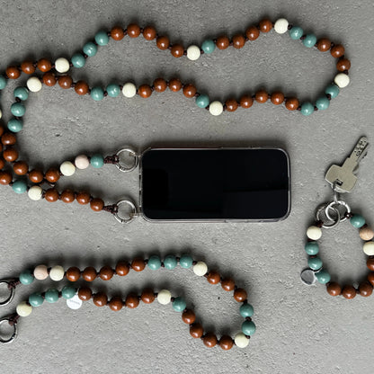 upbeads as phone strap keychain set in 3 different sizes with brown, sage, and cream FSC wooden beads, shown laid out on a gray textured surface alongside a smartphone, keys.
