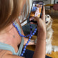 Person taking a photo wearing upbeads wisteria crossbody  of a dog indoors.