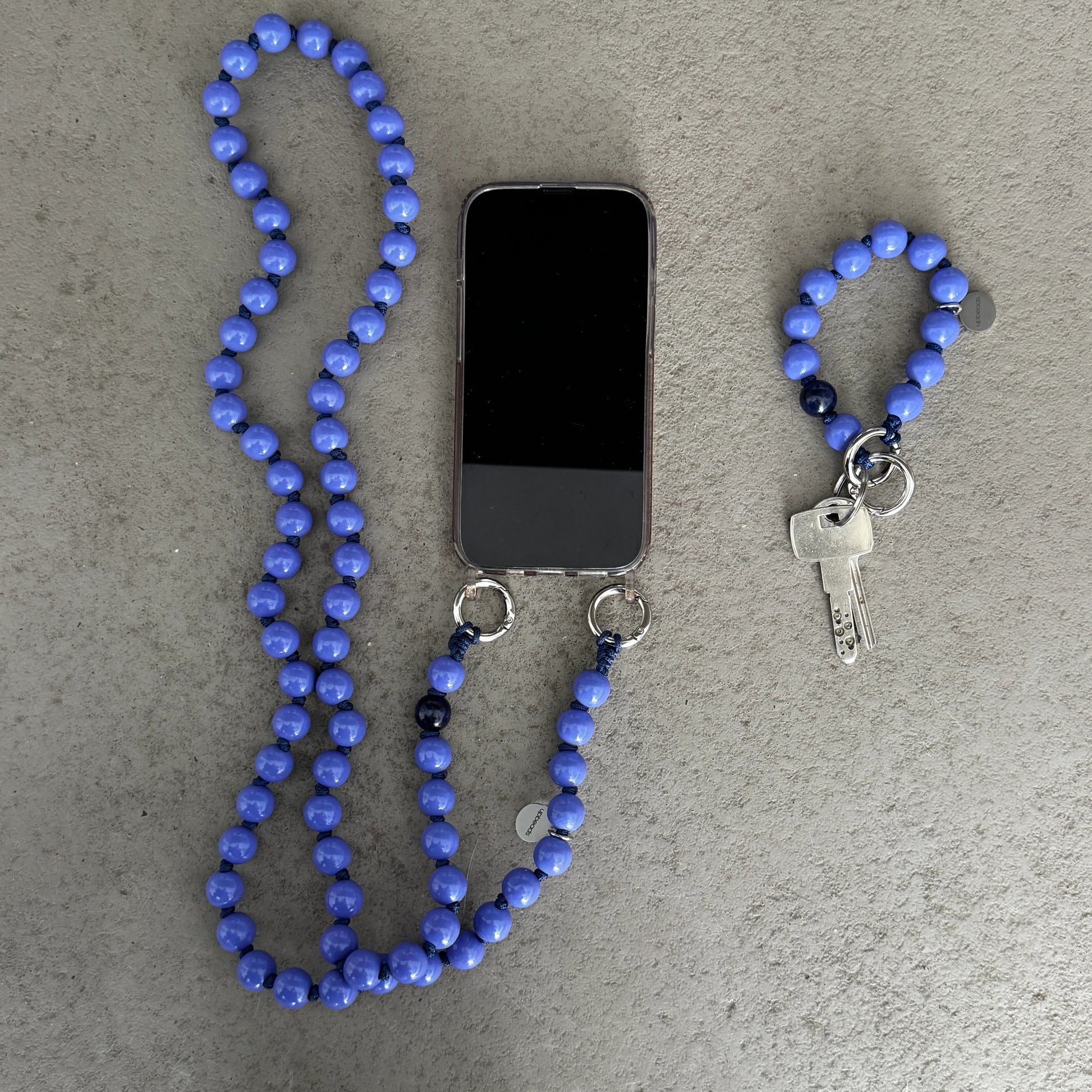 violet Blue wood beaded upbeads crossbody chain as a phone holder and keychain on a gray surface
